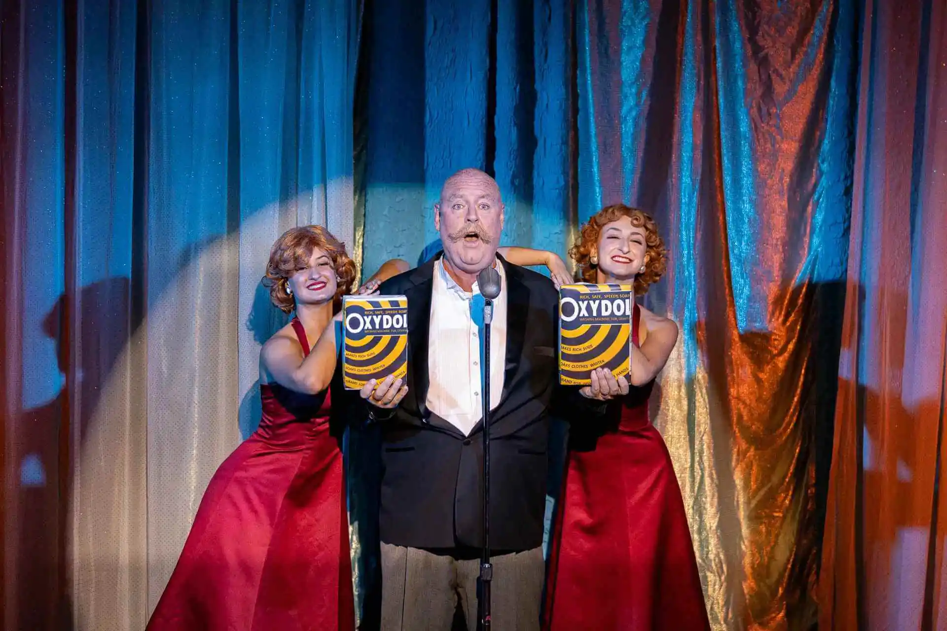 Performing Arts + Theaters Two women in red dresses and a man in a tuxedo perform on a colorful stage