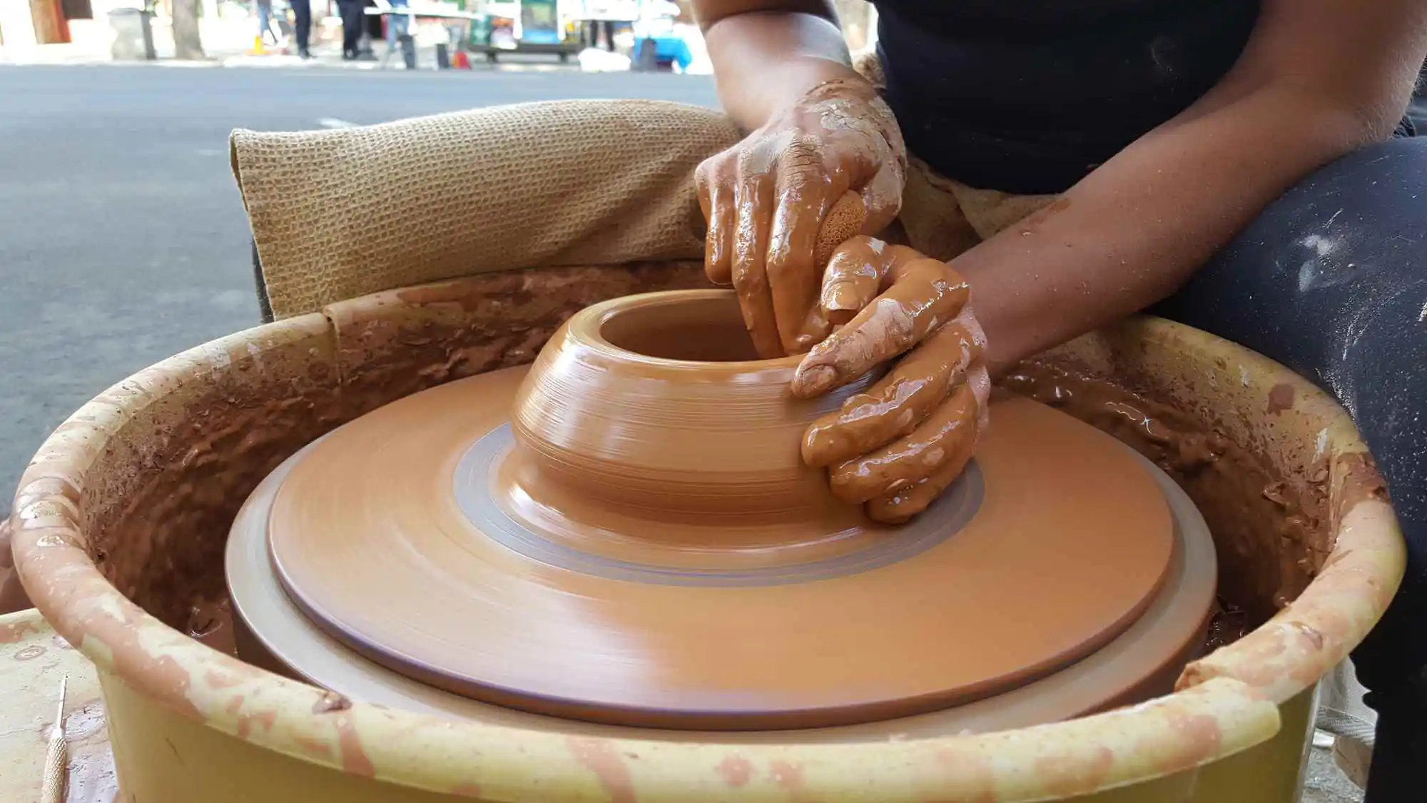 Workshops + Art Studios Close-up of hands sculpting a clay pot on a pottery wheel